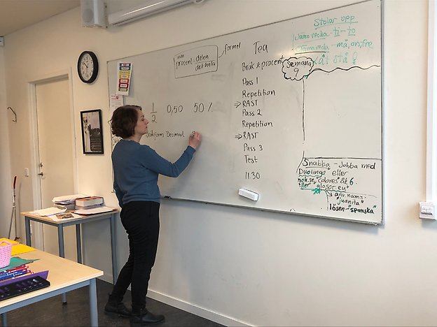 En bild på läraren Tea Karlsson som står i ett klassrum och skriver på en whiteboard.